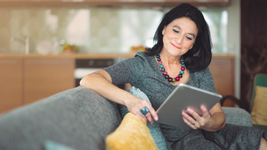 A women is sitting at a table with her laptop open while she is looking off smiling.